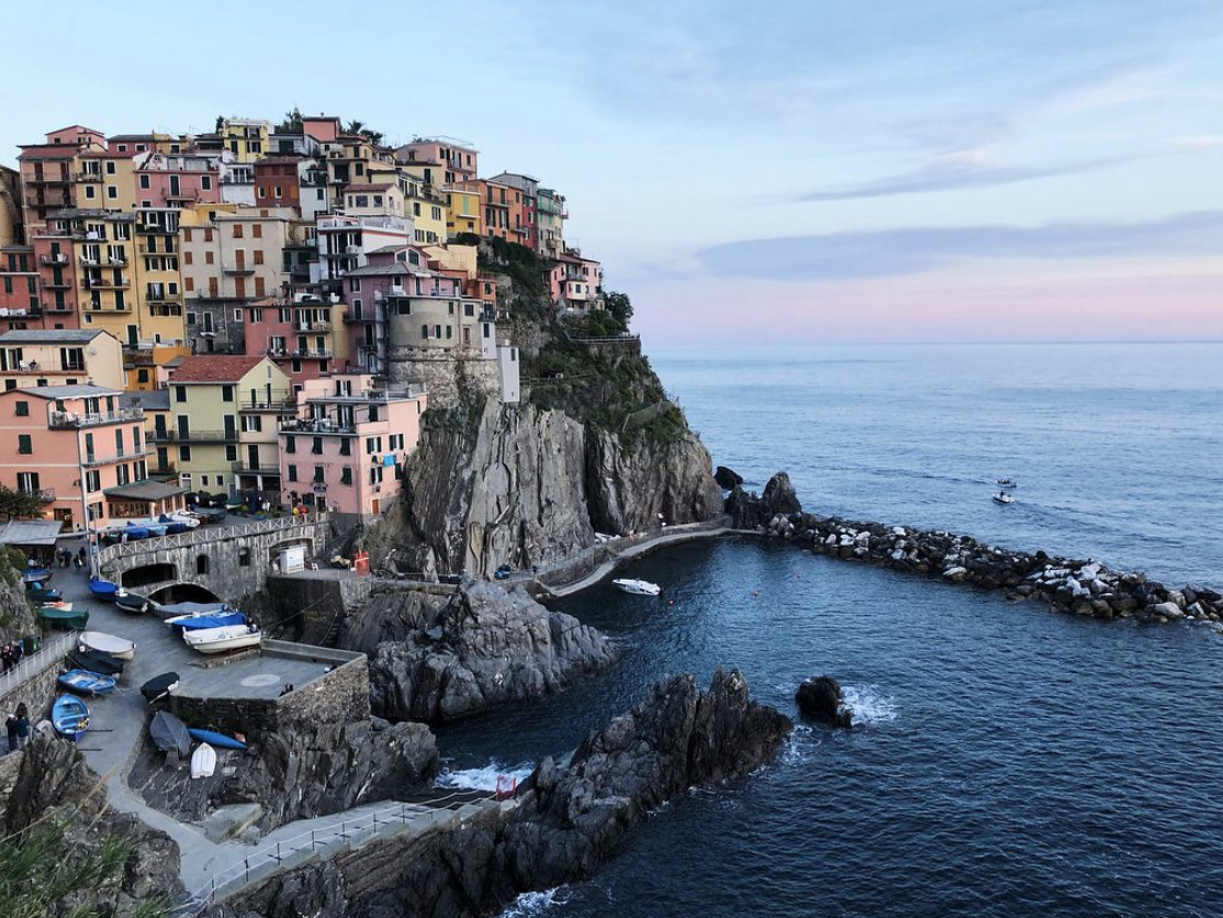 the colorful homes of Cinque Terre rise on a cliff overlooking the ocean at sunset the colorful homes of Cinque Terre rise on a cliff overlooking the ocean at sunset
