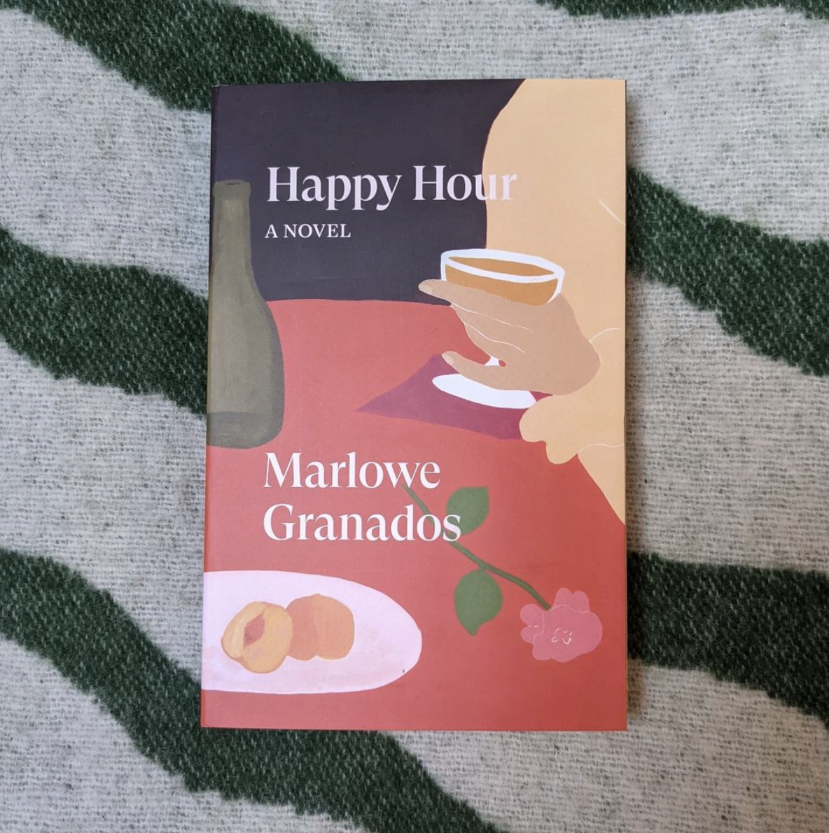a colorful illustrated paperback copy of ''happy hour'' sits flat against a funky striped rug or blanket a colorful illustrated paperback copy of ''happy hour'' sits flat against a funky striped rug or blanket