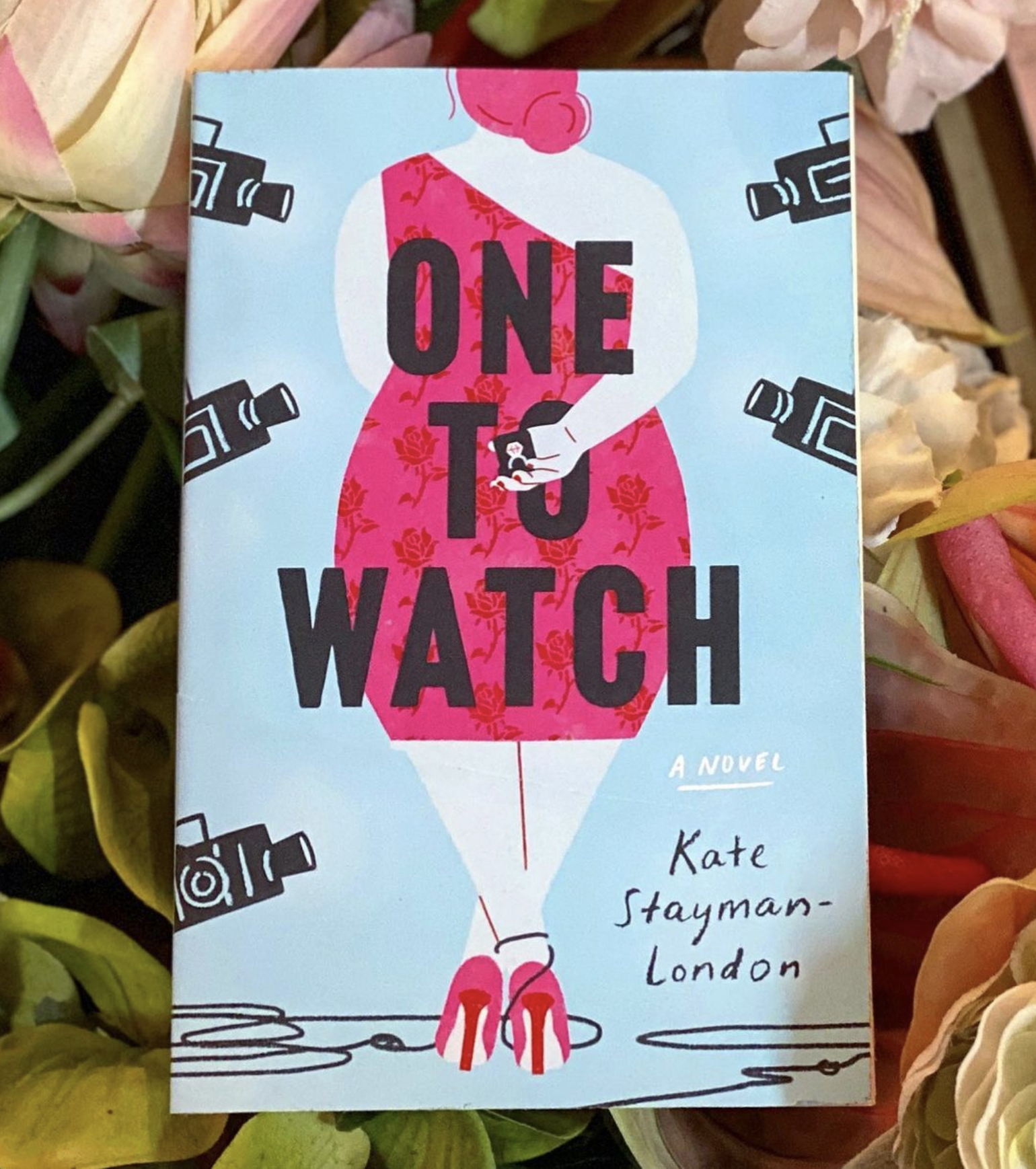 a hardcover copy of one to watch lays against a bed of flowers a hardcover copy of one to watch lays against a bed of flowers