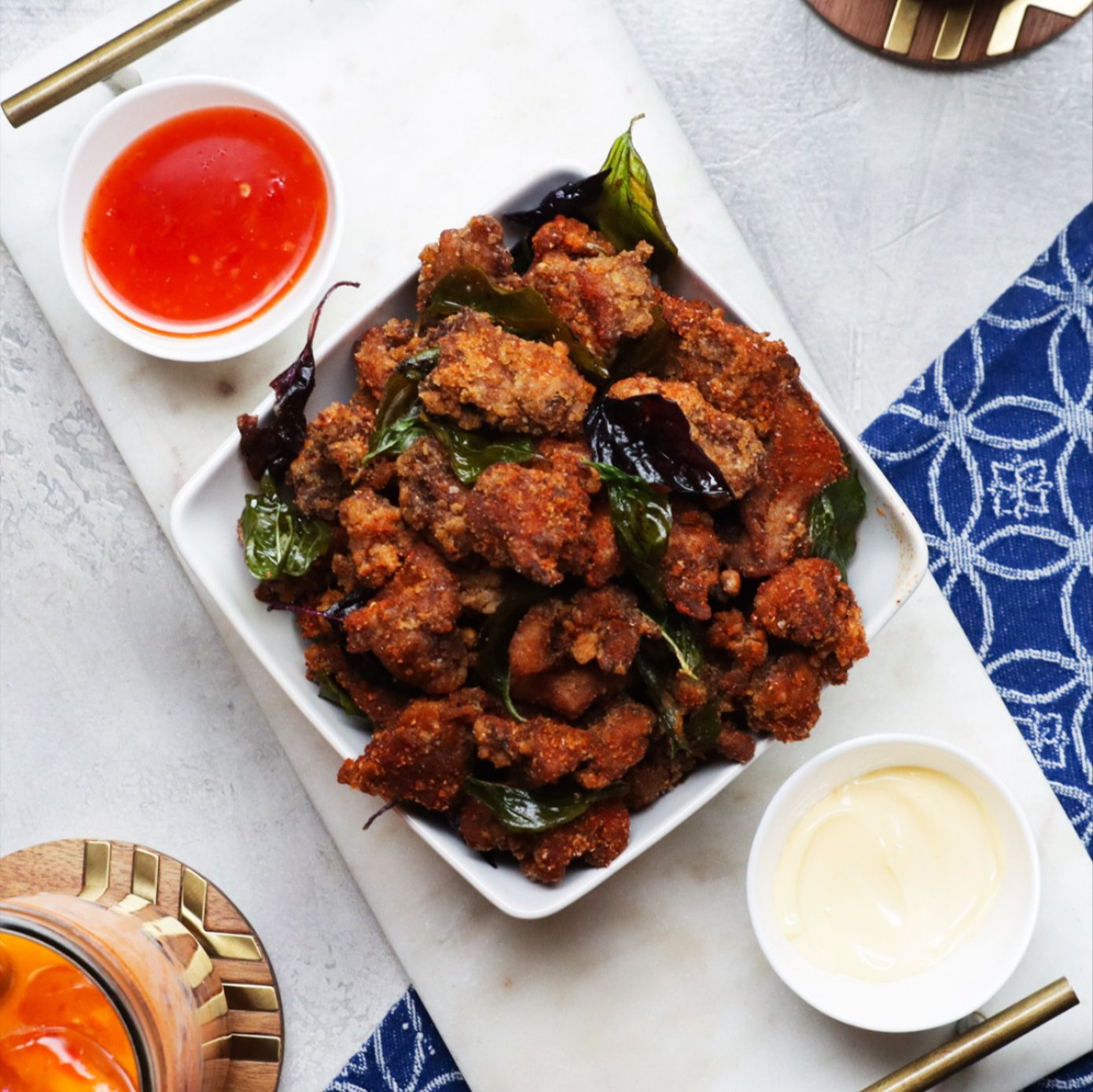 a pretty tablescape with a bowl of crunchy fried chicken bites atop a marble tray and multiple sauces