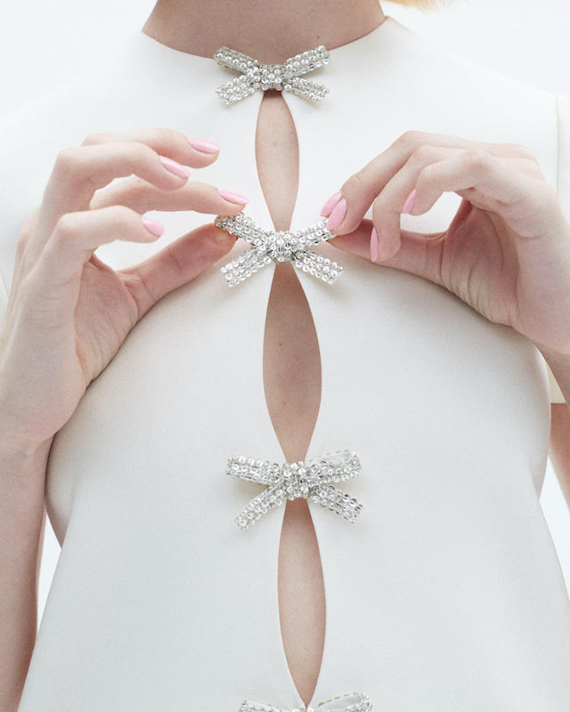A person wearing a white top with rhinestone bows.