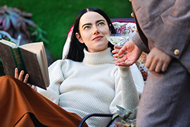 Emma Stone holding a book sitting in a chair.