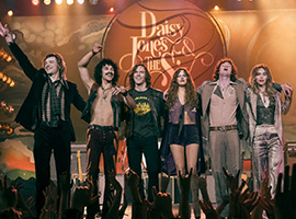 A group of people with their arms around each other on stage in front of a crowd.