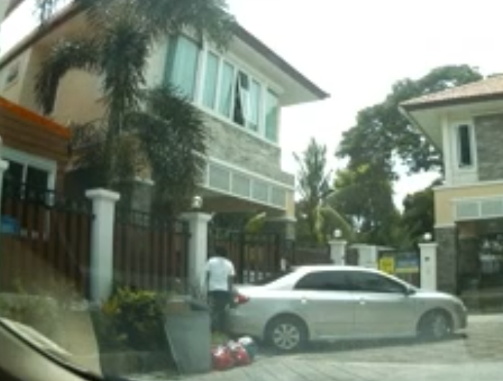A still from a video showing Nueng from behind, standing by the trunk of the Toyota