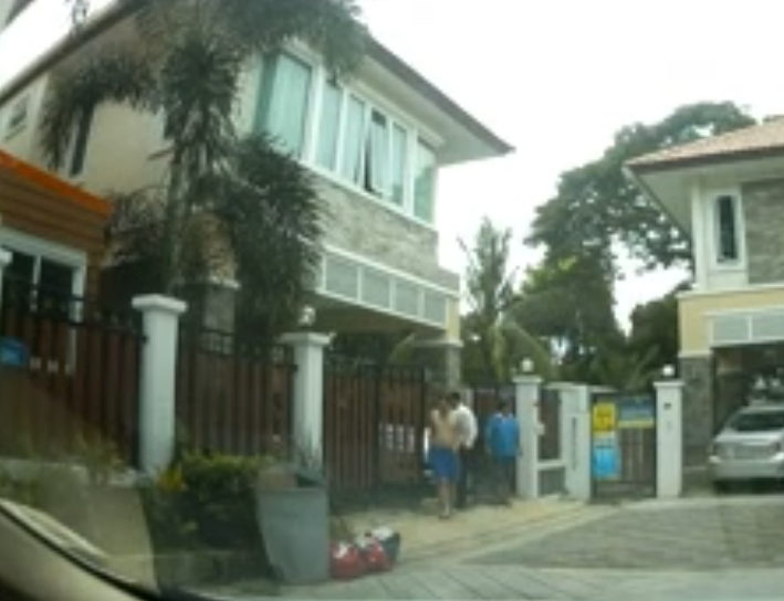 Cazes emerging from the gate in front of his house wearing blue shorts