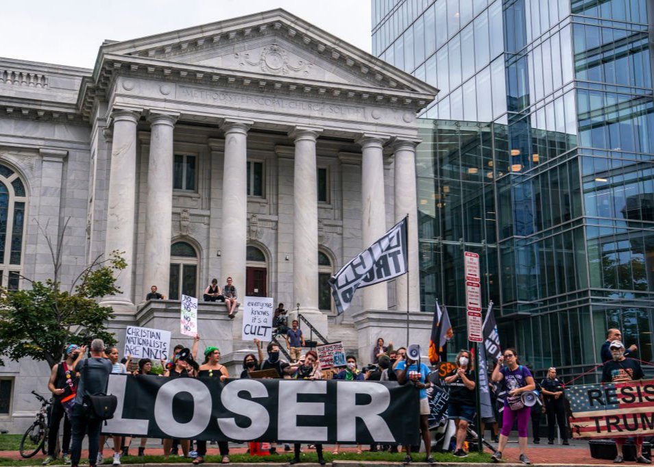 Protesters outside a state building hold large banners that read LOSER and RESIST TRUMP