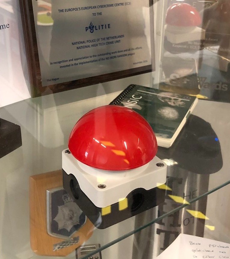 A red plastic button on a glass shelf next to a notebook.