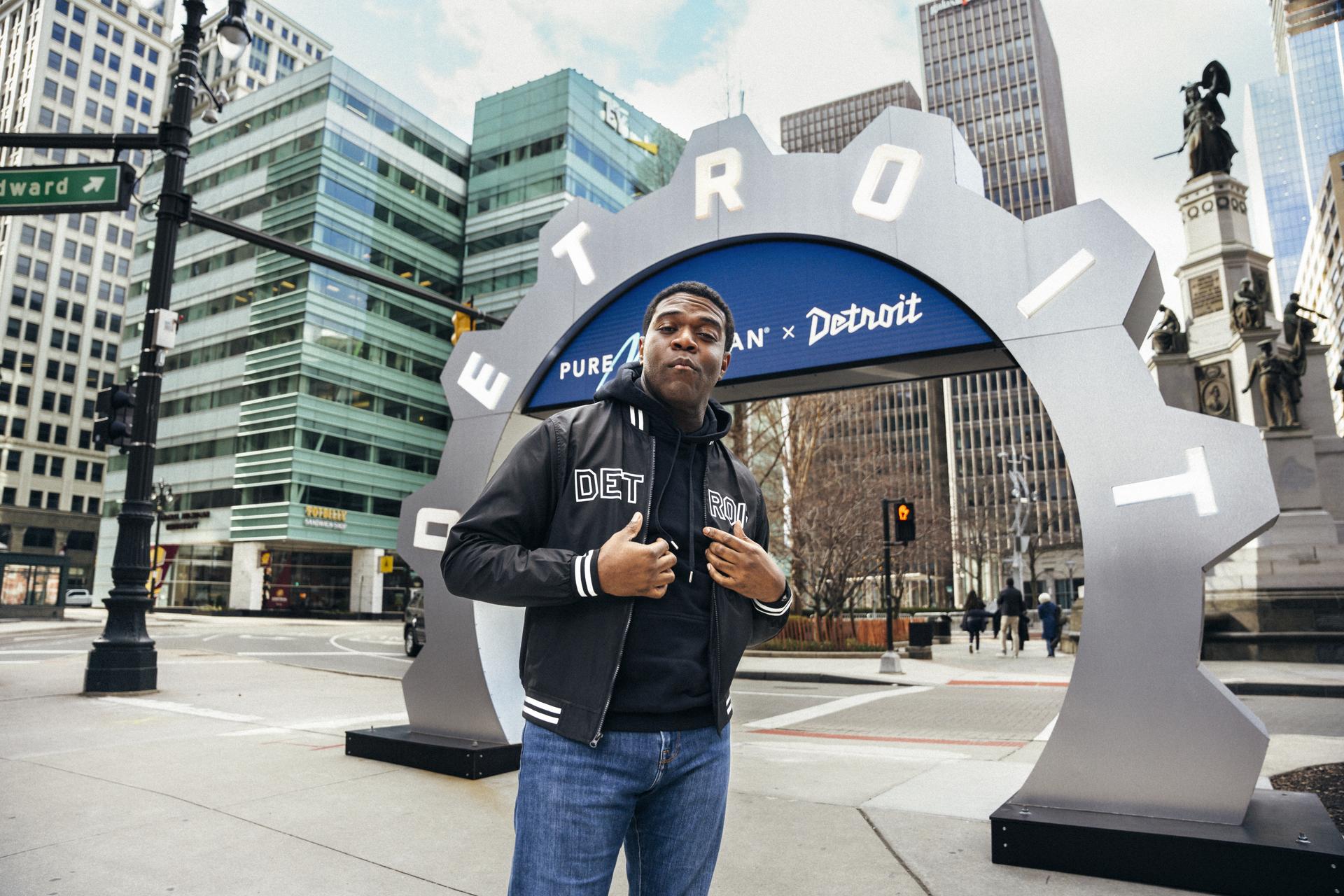 Detroit native Sam Richardson poses in front of a Pure Michigan and Detroit sign in the shape of a gear.