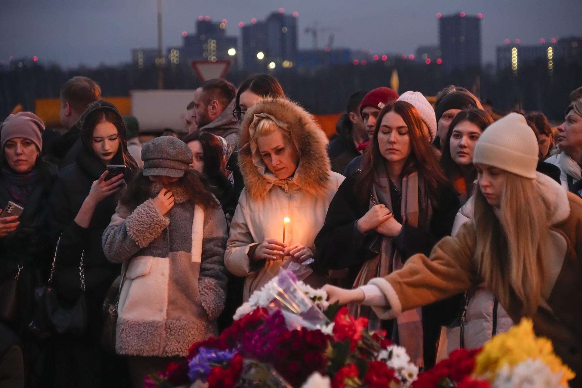 People lay flowers and light candles standing next to the Crocus City Hall, on the western edge of Moscow, Russia.