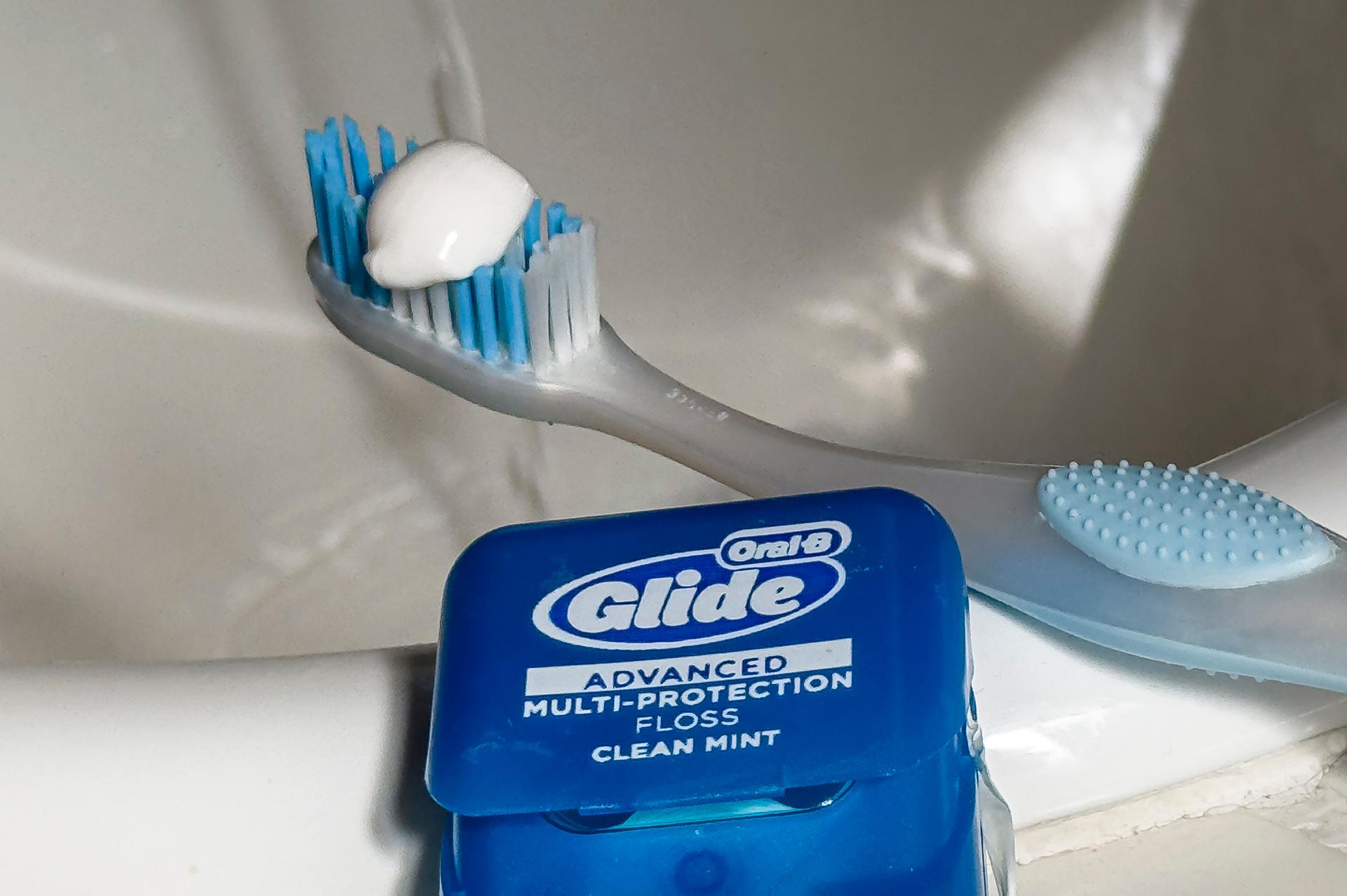 Photo of a toothbrush with toothpaste on the bristles beside a package of dental floss.