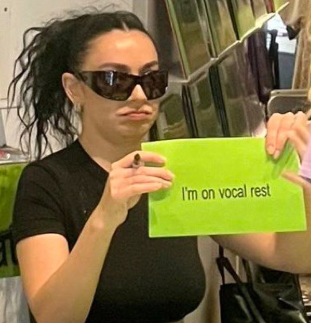 Charli XCX holds a sign reading, ''I'm on vocal rest,'' during a meet and greet promoting her new album Brat.