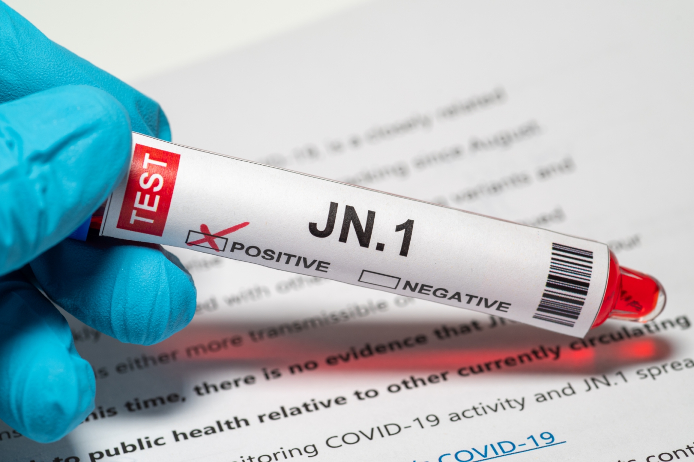 A gloved hand holds a vial of fluid labelled JN.1