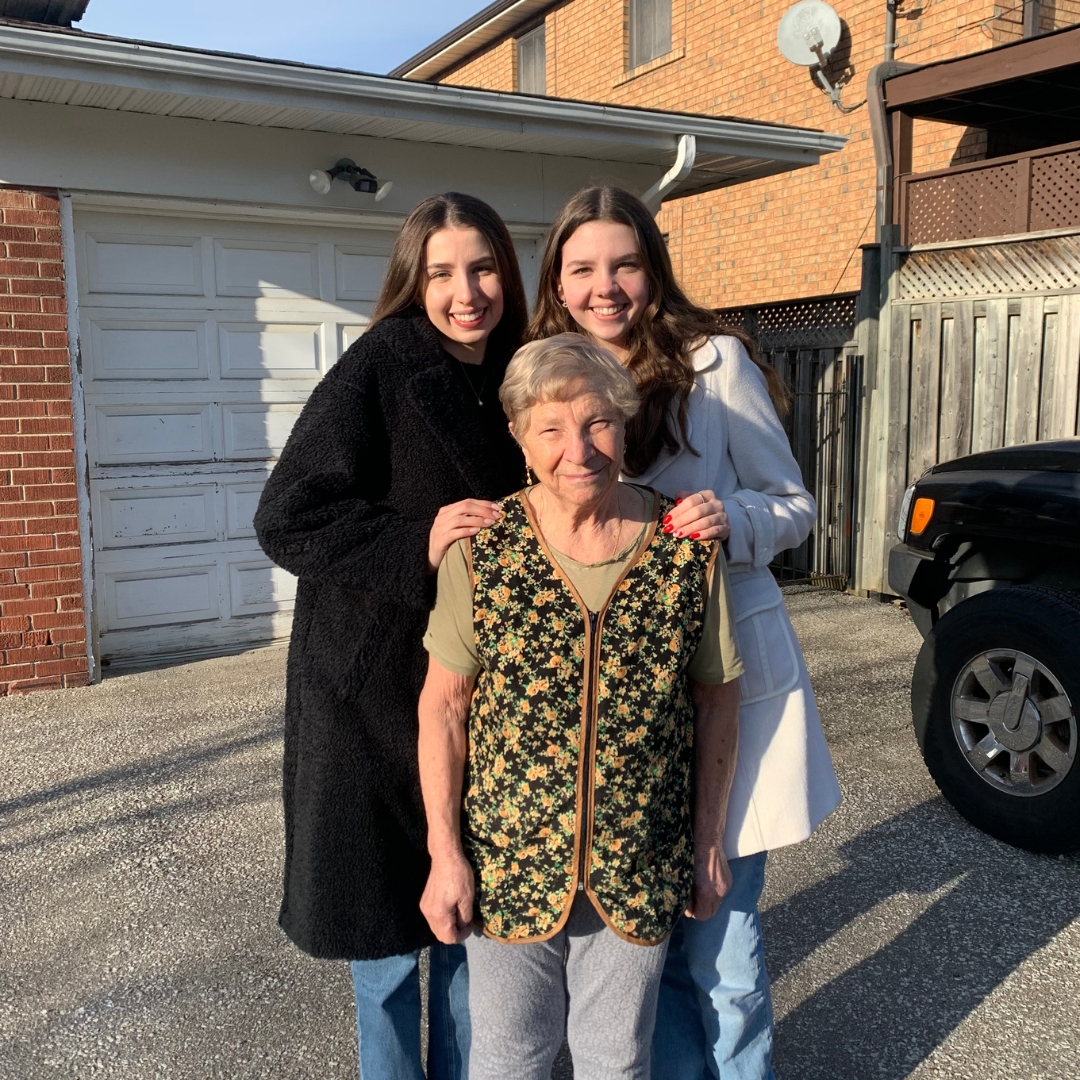 A photo of two young women posing with their nonna.