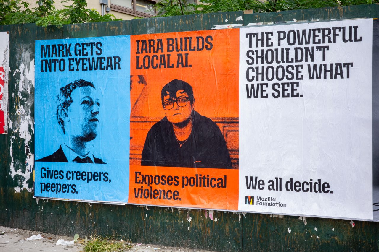 Three posters are pasted side by side on a weathered green construction wall. The blue poster on the left reads "Mark gets into eyewear. Gives creepers, peepers." above a black-and-white photo of Mark Zuckerberg. The orange poster in the middle reads "Iara builds local AI. Exposes political violence." above a black-and-white photo of Iara Passos. The white poster on the right reads "The powerful shouldn't choose what we see. We all decide." and has the Mozilla Foundation logo in the bottom corner.