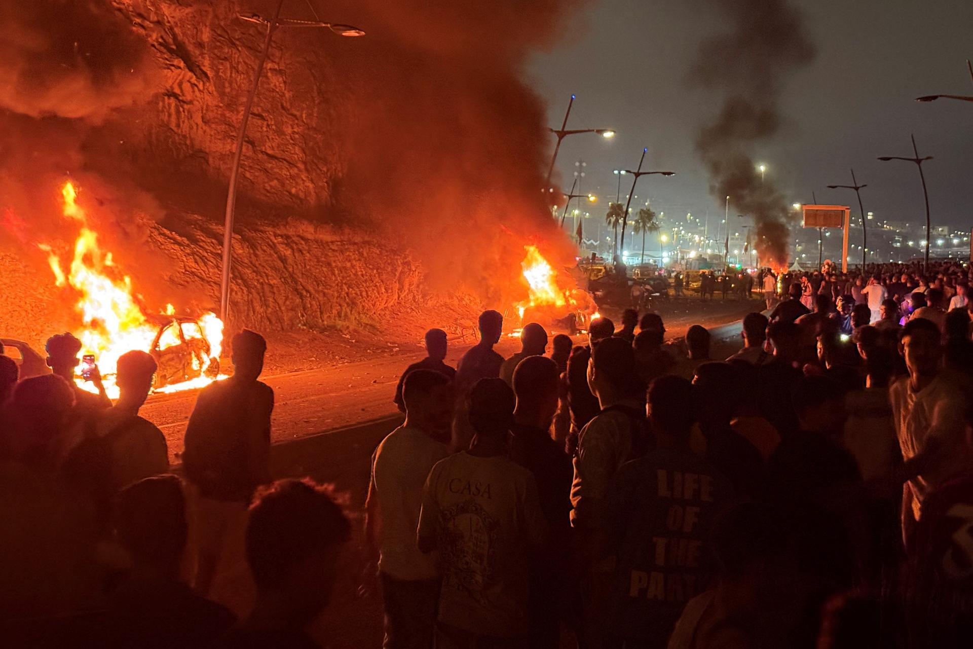 Migrants gather next to burning cars as they wait for a chance to cross to the Spanish enclave of Ceuta