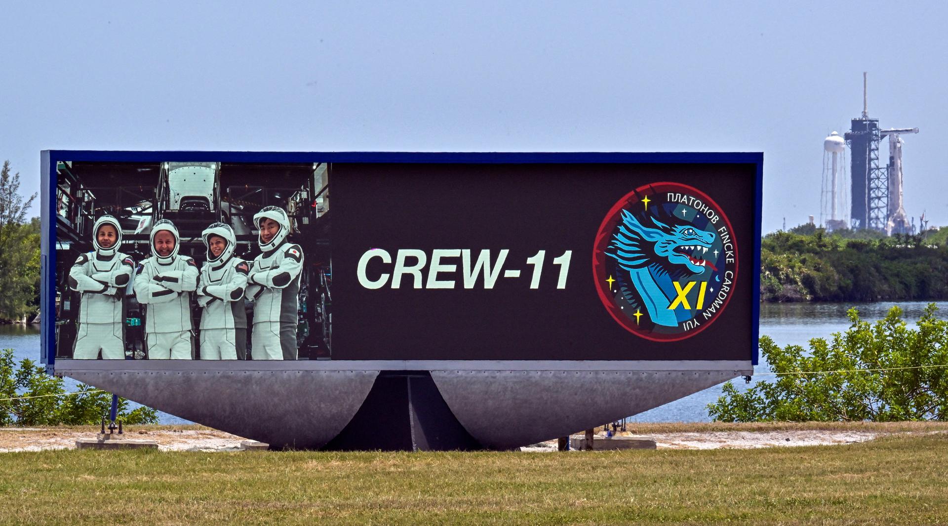 A Falcon 9 rocket behind a countdown clock displaying a photo of NASA's SpaceX Crew-11 members in Cape Canaveral