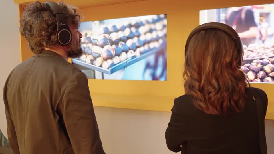 People look at pictures of food at an exhibition while listening to sound on headphones