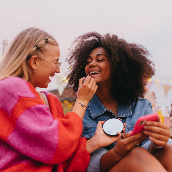 Girls smiling together putting on lipstick