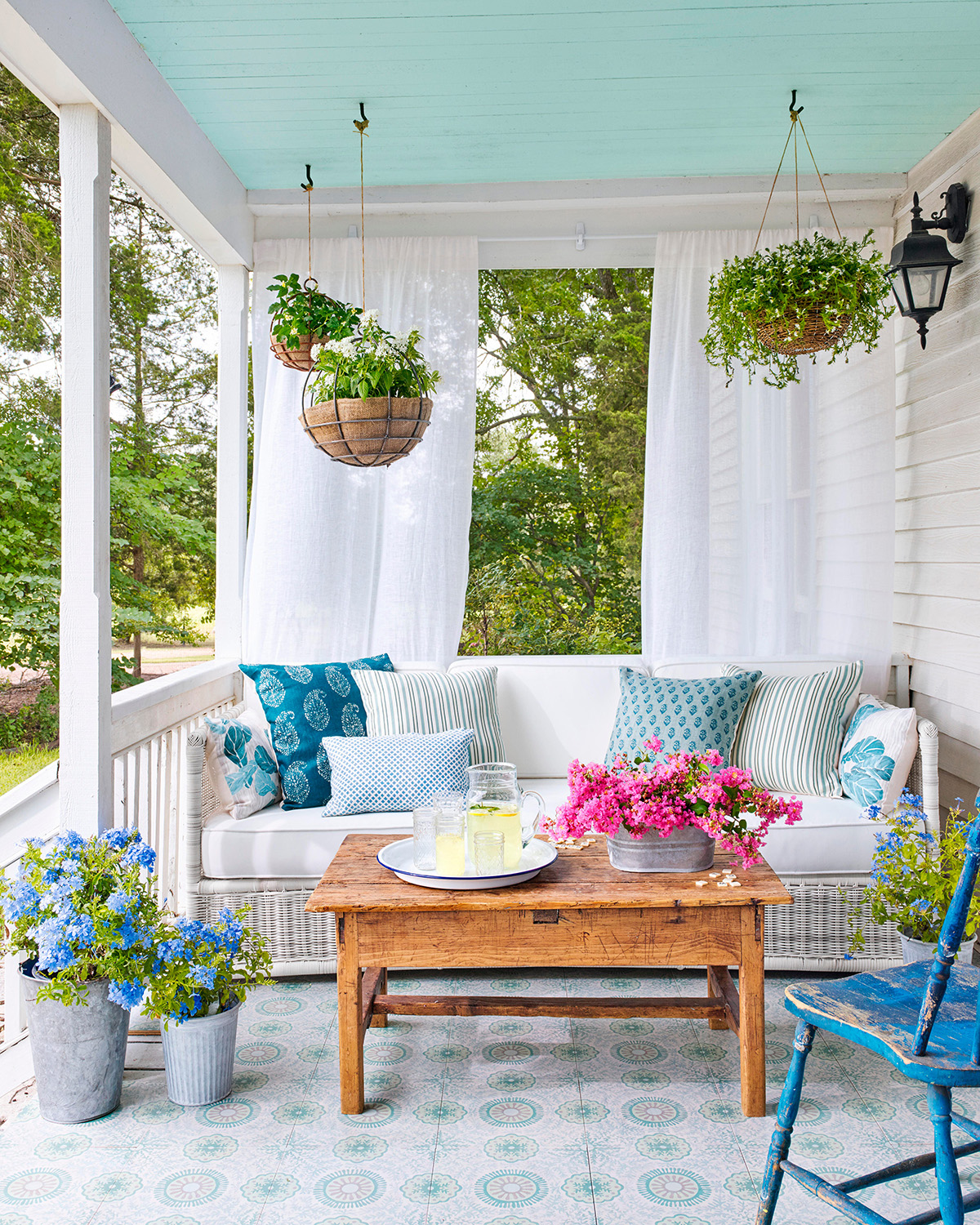 Covered porch with blue ceiling, wicker sofa, gauzy white curtains 