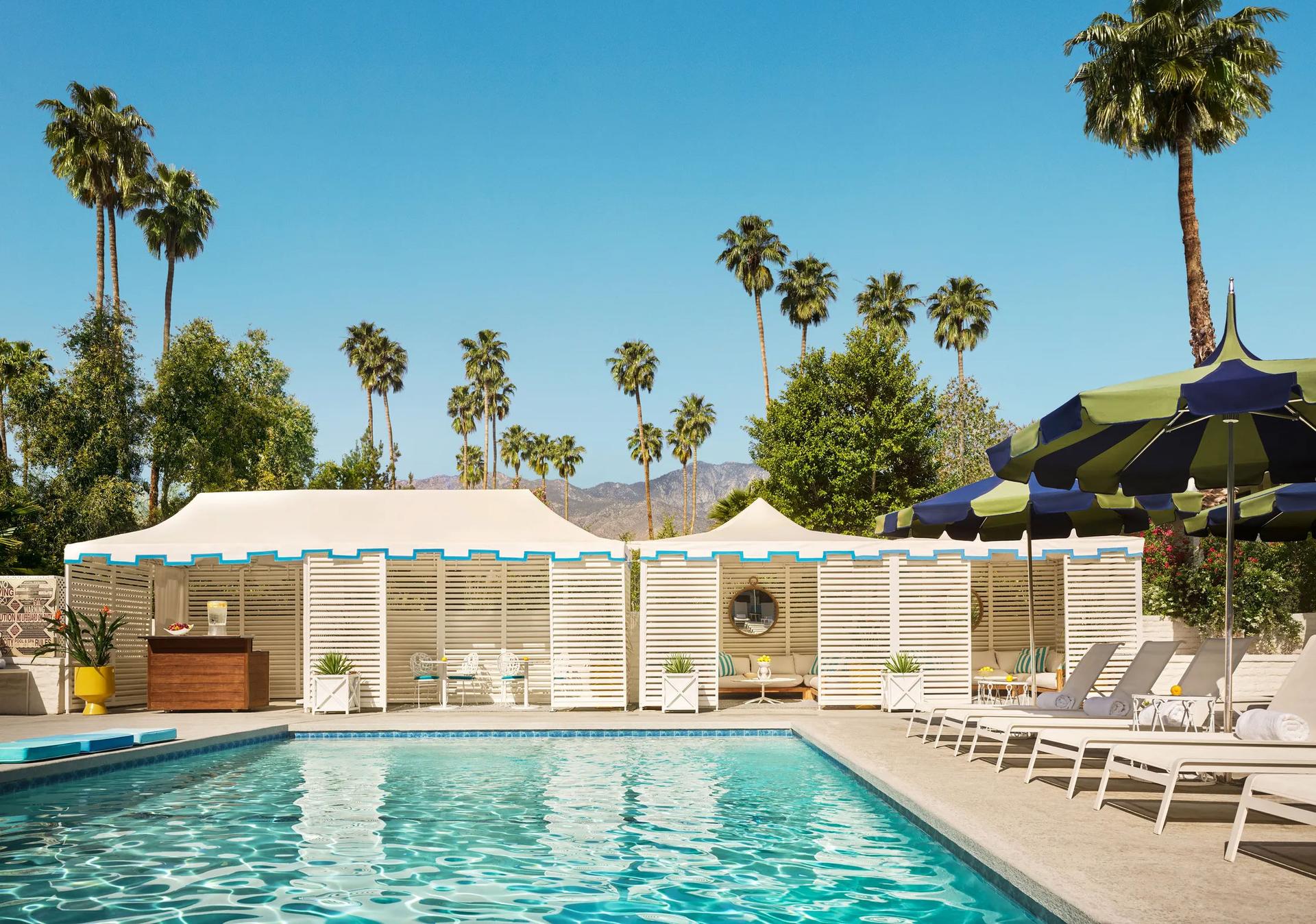 Hotel pool with chairs surrounding it and palm trees in background