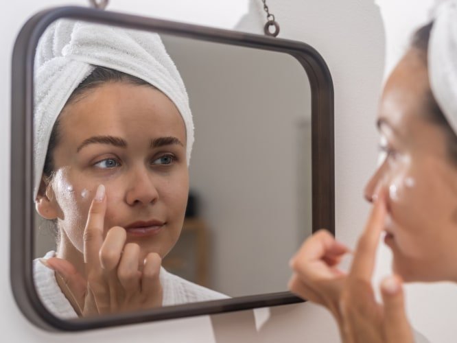 Person applying eye cream in mirror