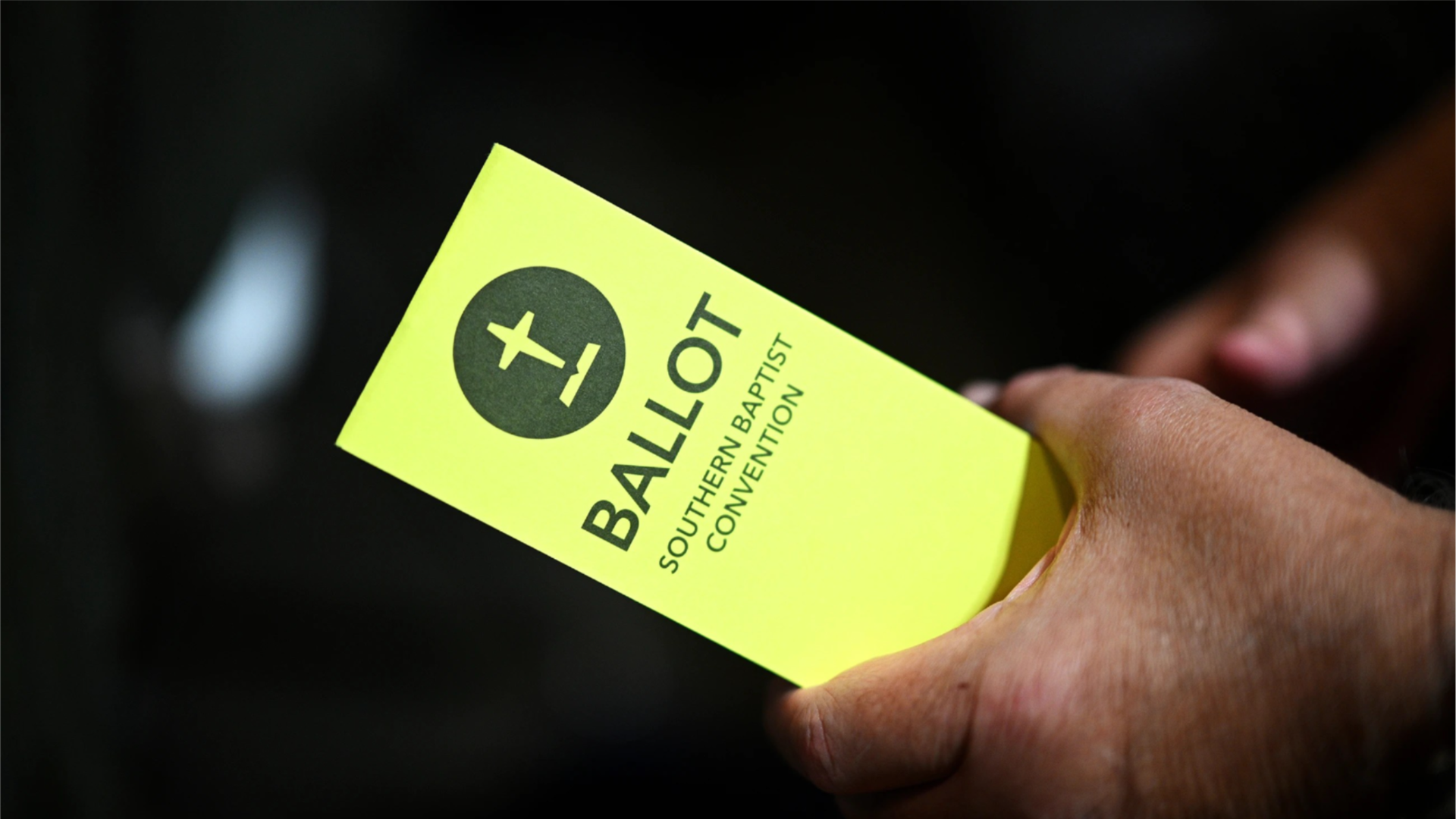 A person holds a yellow paper ballot