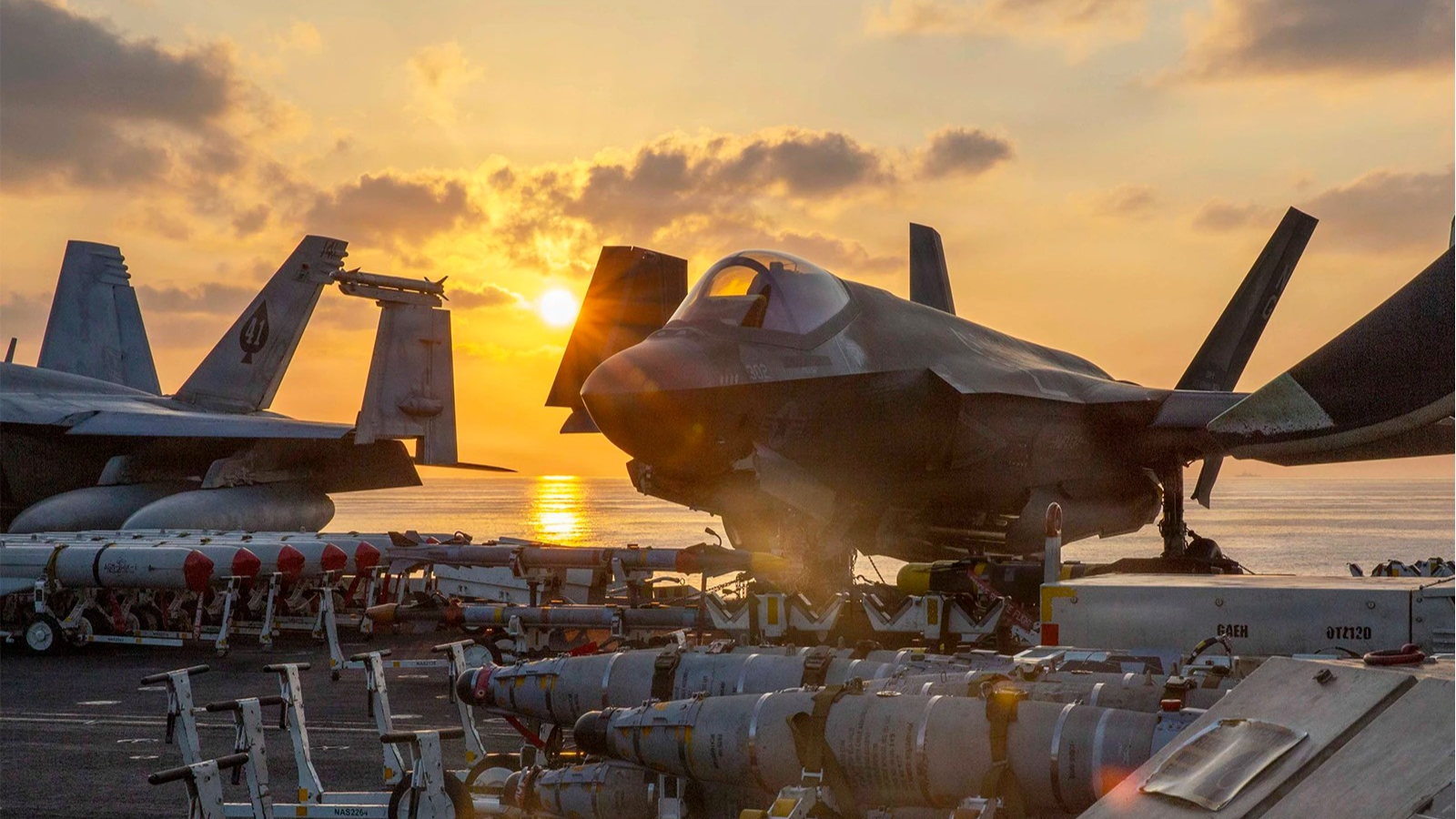 Weapons and a war plane are seen at sunset on a navy ship.