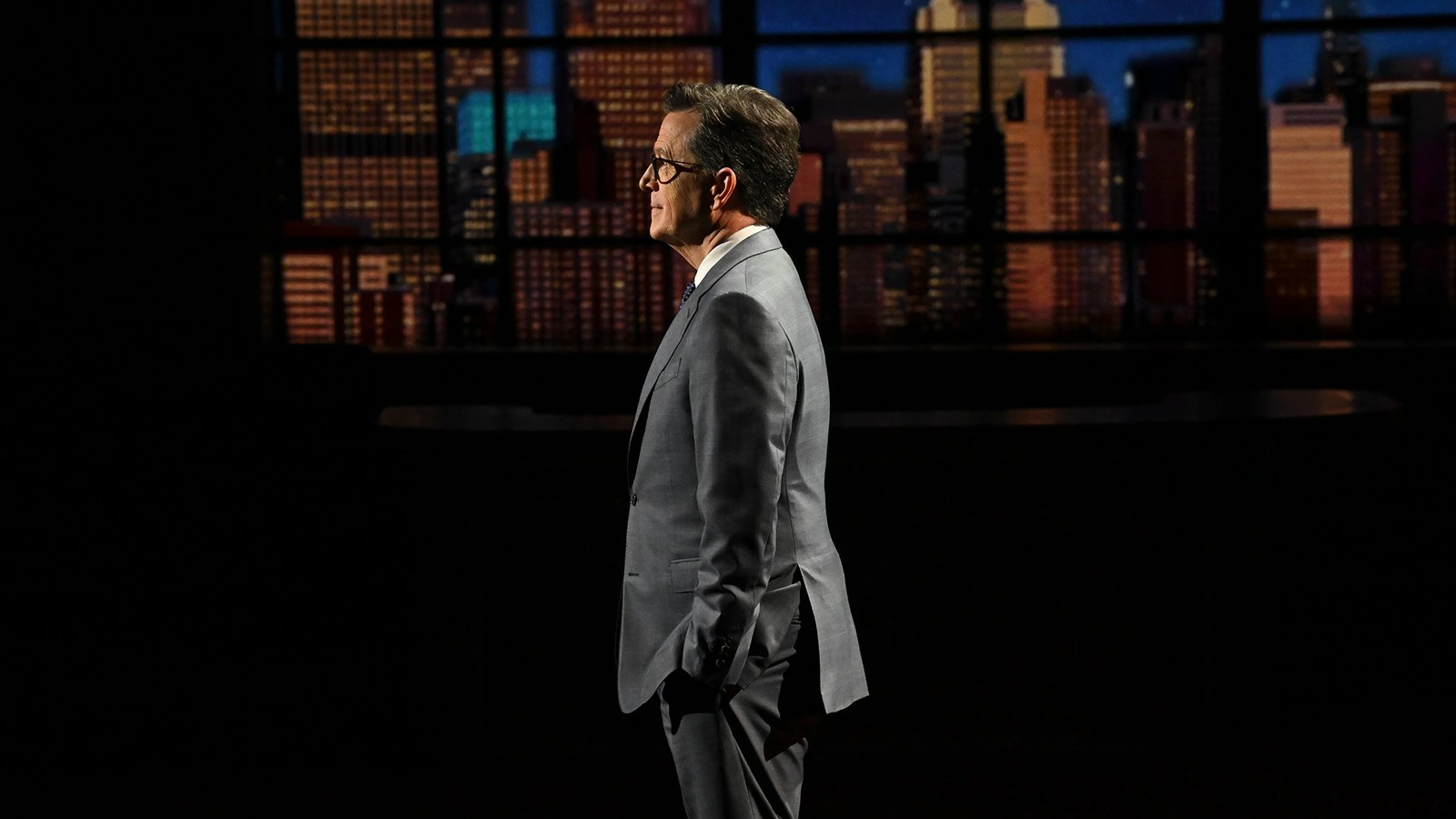 Stephen Colbert stands in front of a skyline.