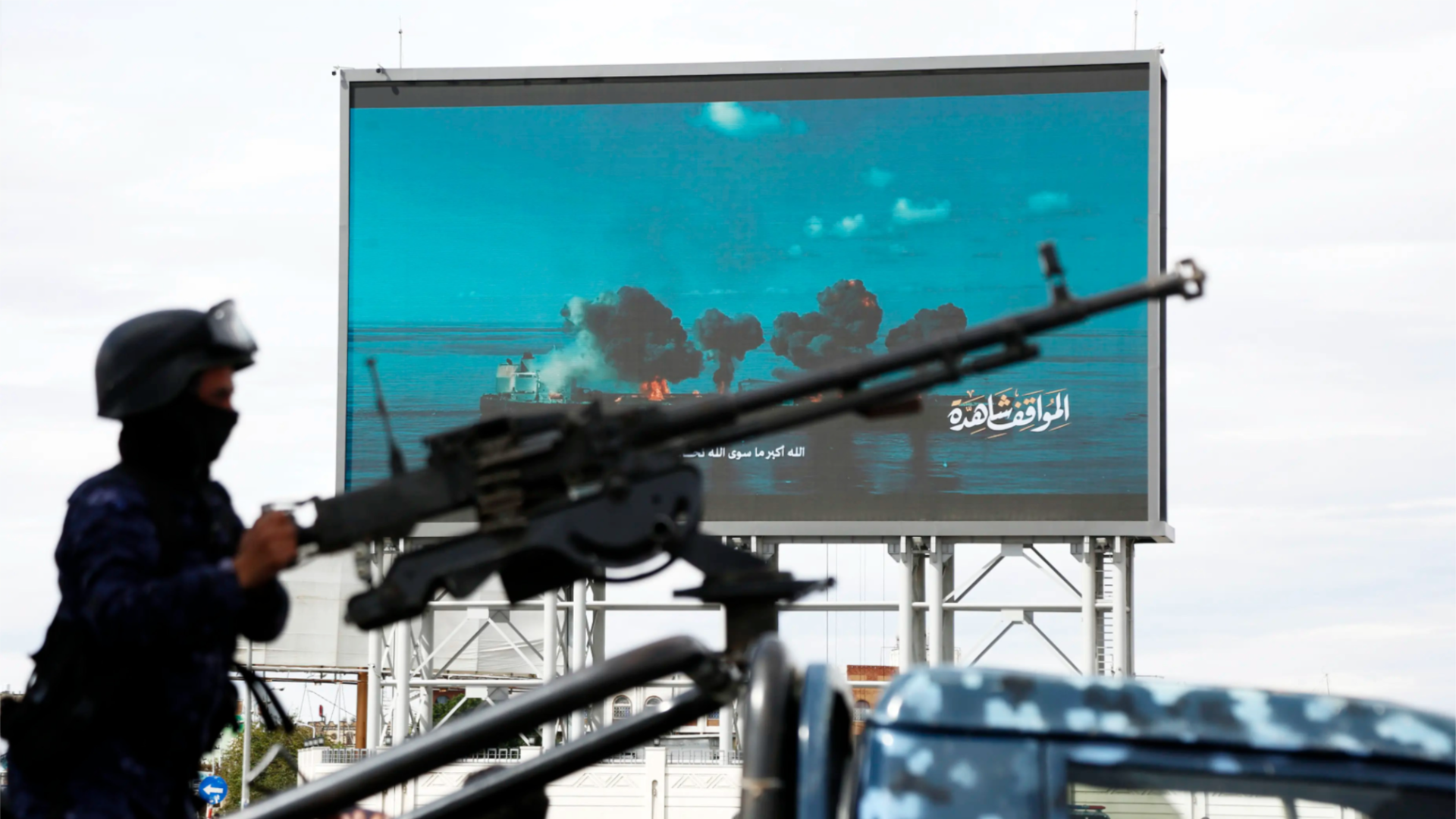 A Yemen's Houthi soldier mans a machine gun mounted on a police vehicle next to a billboard depicting Houthi launching missile and drone attacks.