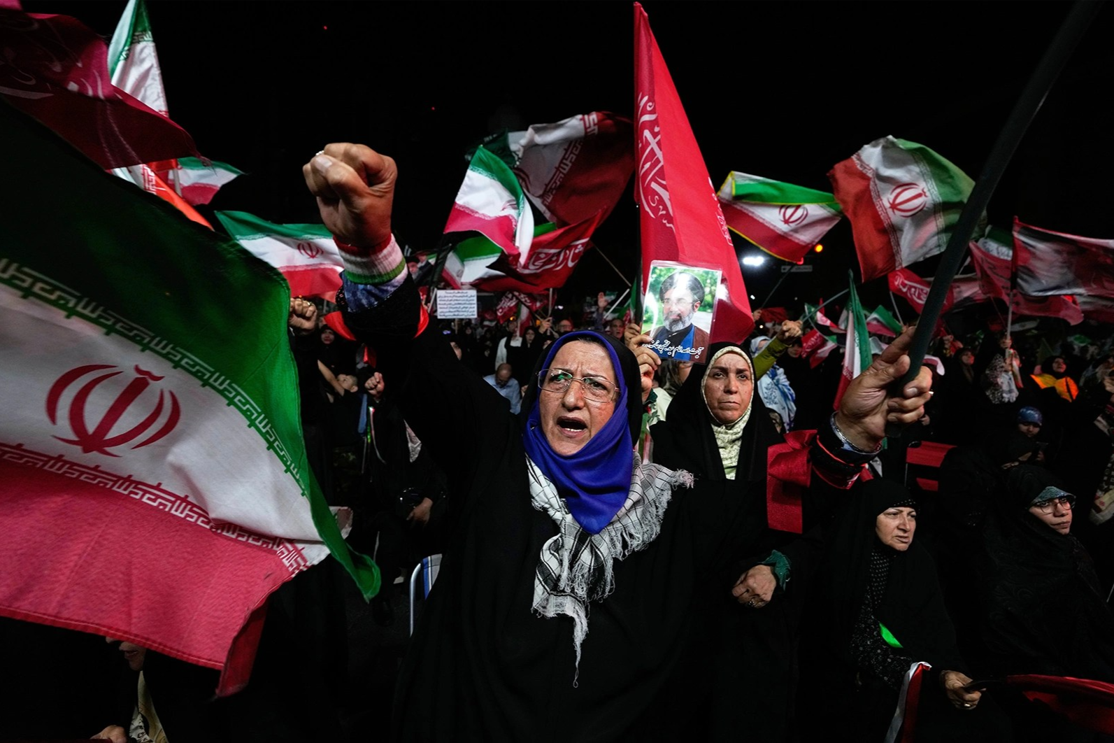 People chant and wave Iranian flags during a protest at night.