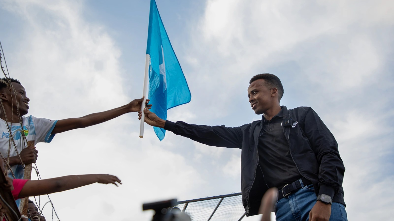 Omar Artan, right, holds out his hand to grab a Somali flag, which a fan on the left side of the photo is also reaching out and holding.