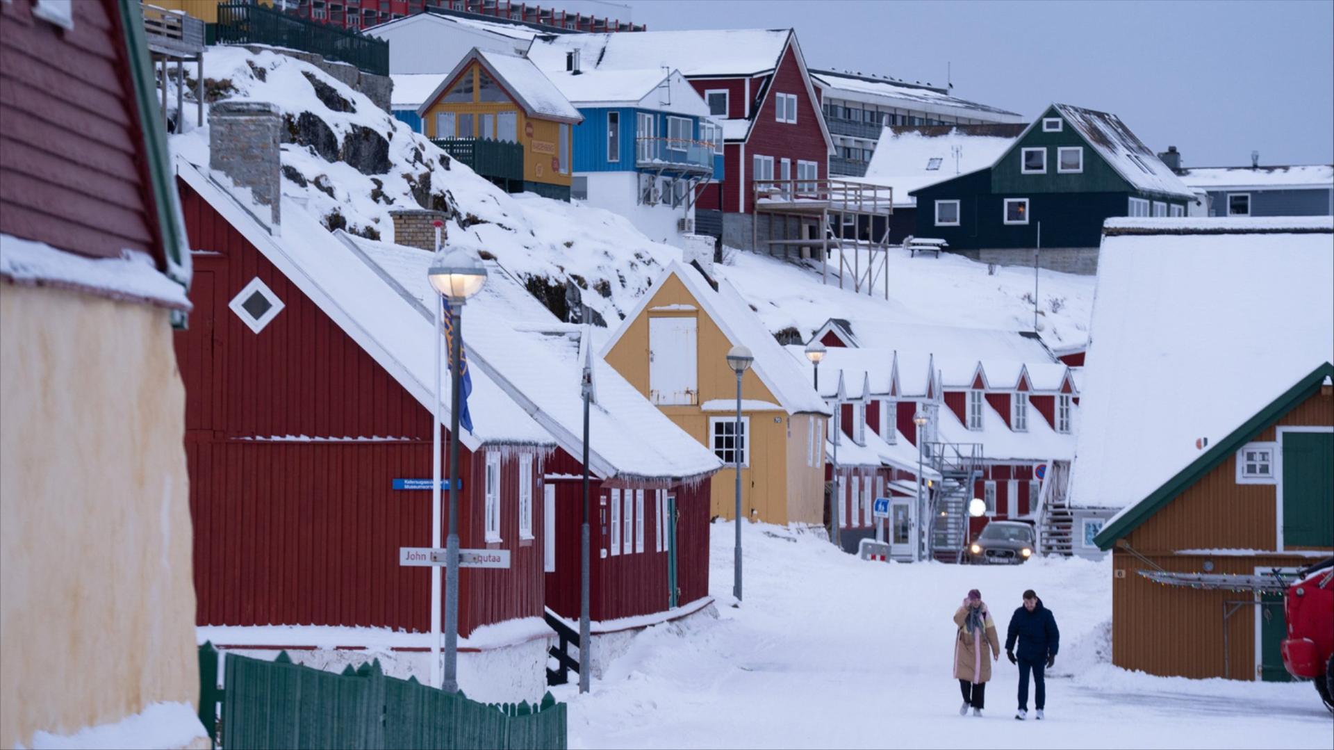 Two people walk among brightly painted houses in the snow