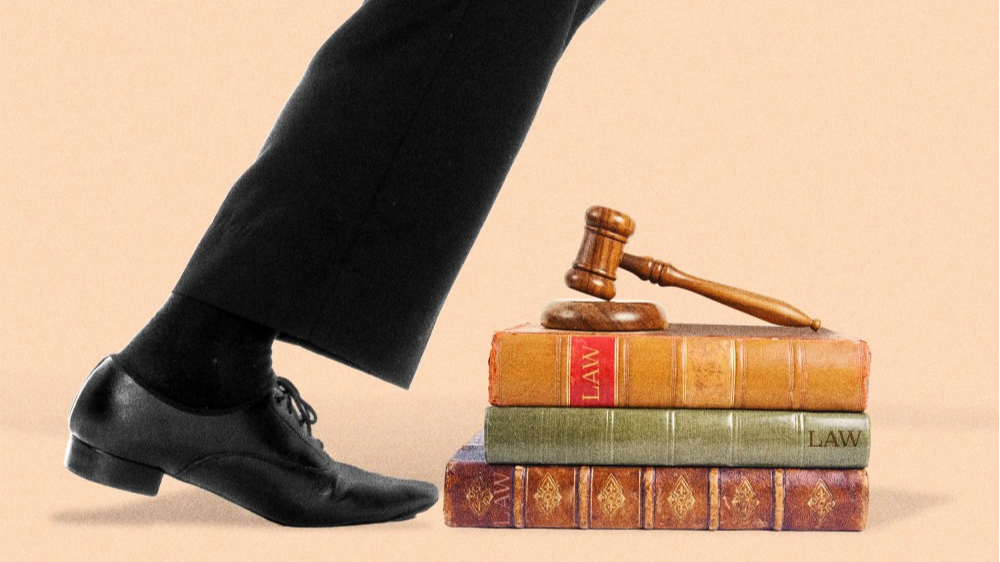 Photoillustration of a man in a business suit tripping over law books and a gavel.