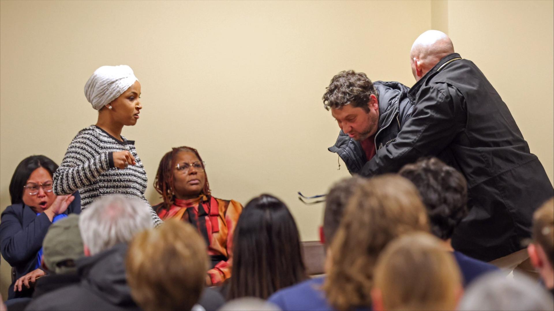 Rep. Ilhan Omar raises her fist while security tackles a person