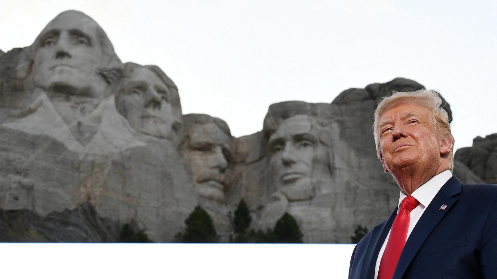 Donald Trump stands with Mount Rushmore in the background. He is on the right of the monument, making it look like he is the fifth face on the rocks.
