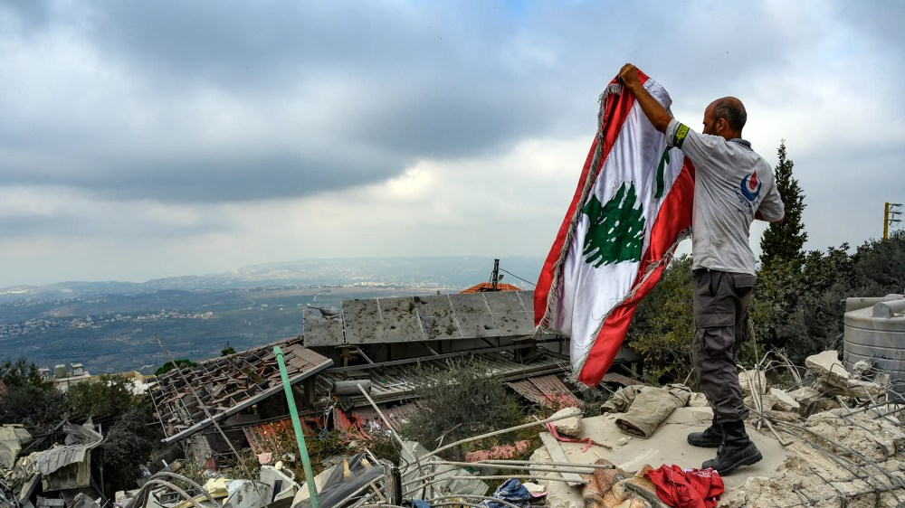 A member of the The Islamic Health Organization, an emergency response organization, raises the Lebanese flag amid rubble that remains from an Israeli airstrike on Oct. 13, 2024 in Deir Billa, Lebanon.