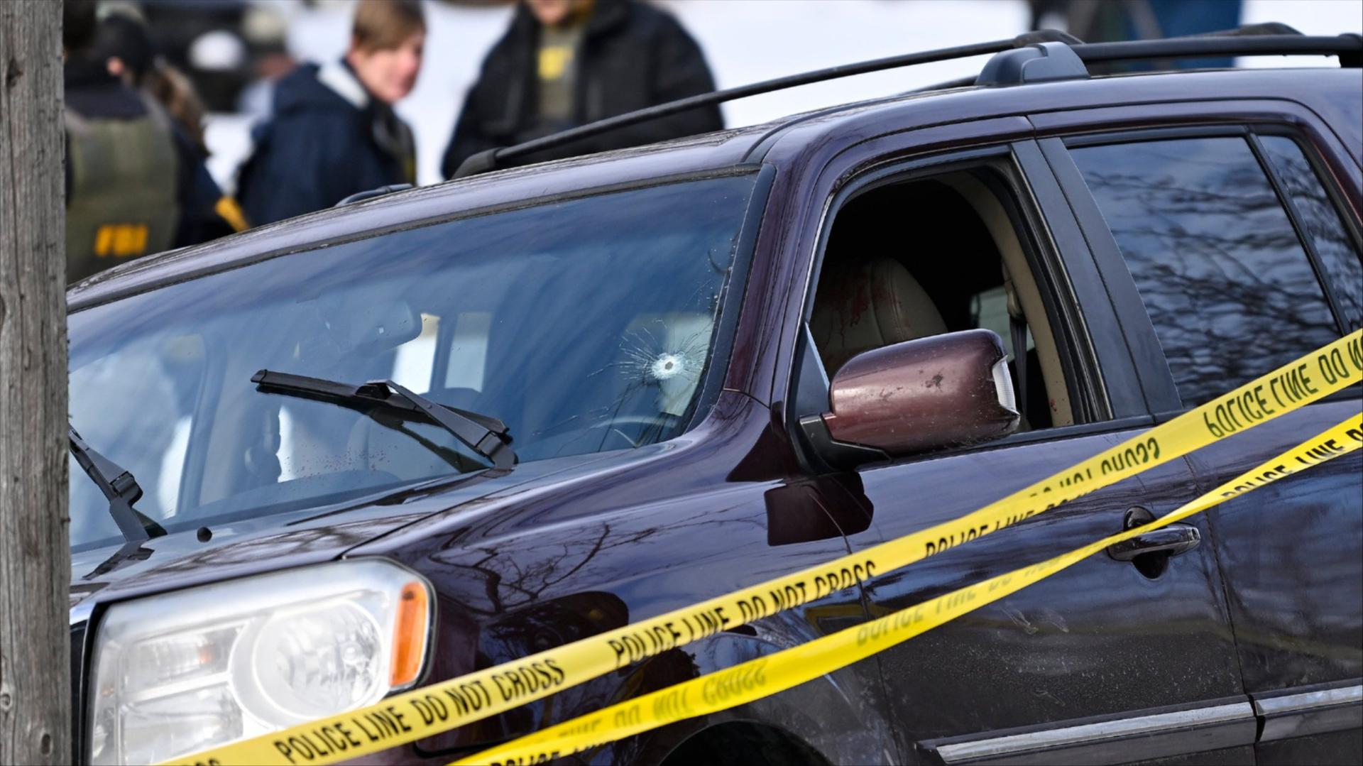 A car with a bullet hole in the windshield surrounded by yellow police tape.