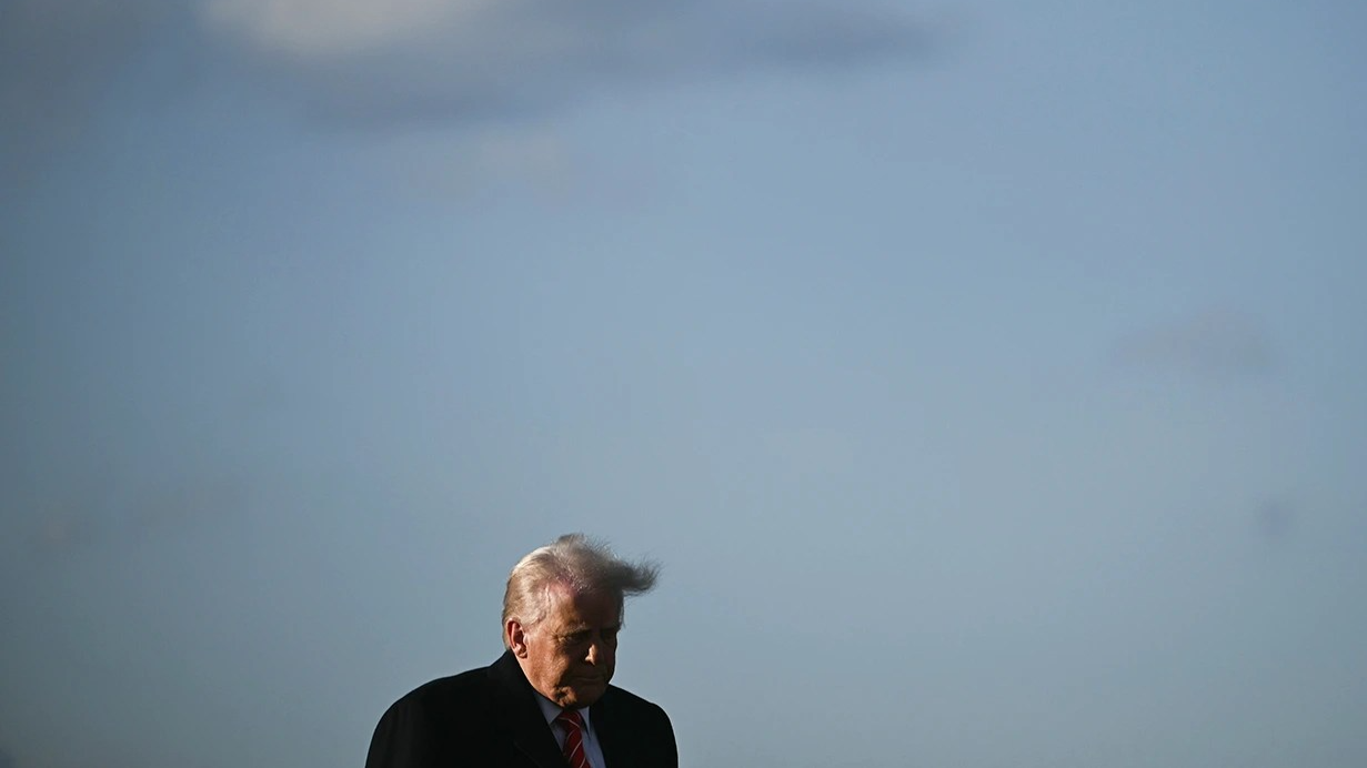 Donald Trump, seen from the shoulders up, is seen against a partly cloudy sky.
