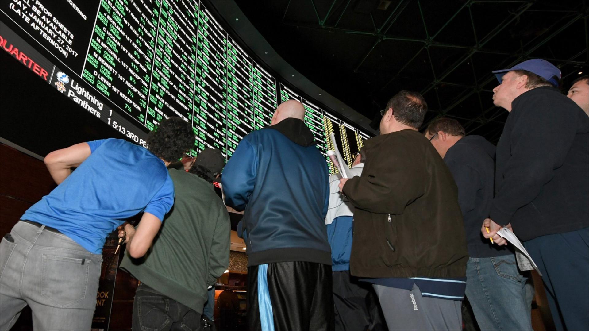 People look up toward a betting odds video board