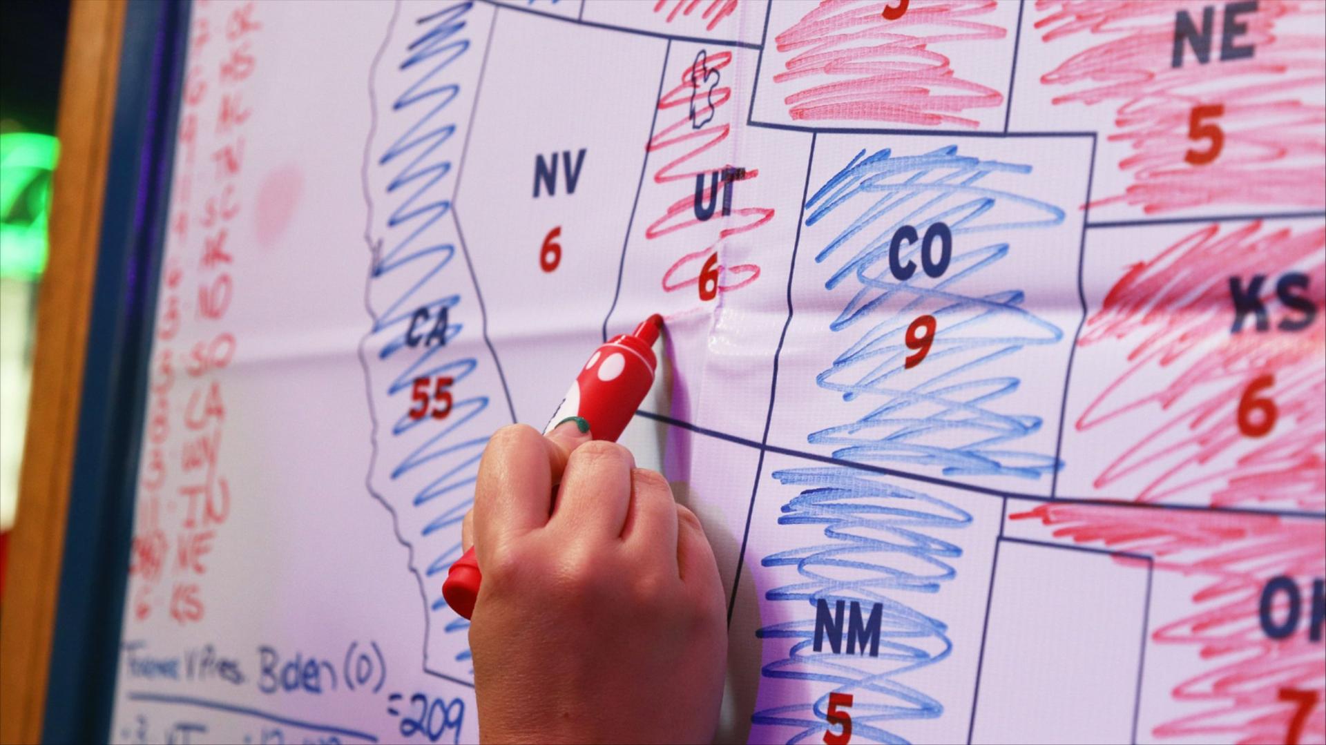 A hand holding a red marker colors Utah red on a map