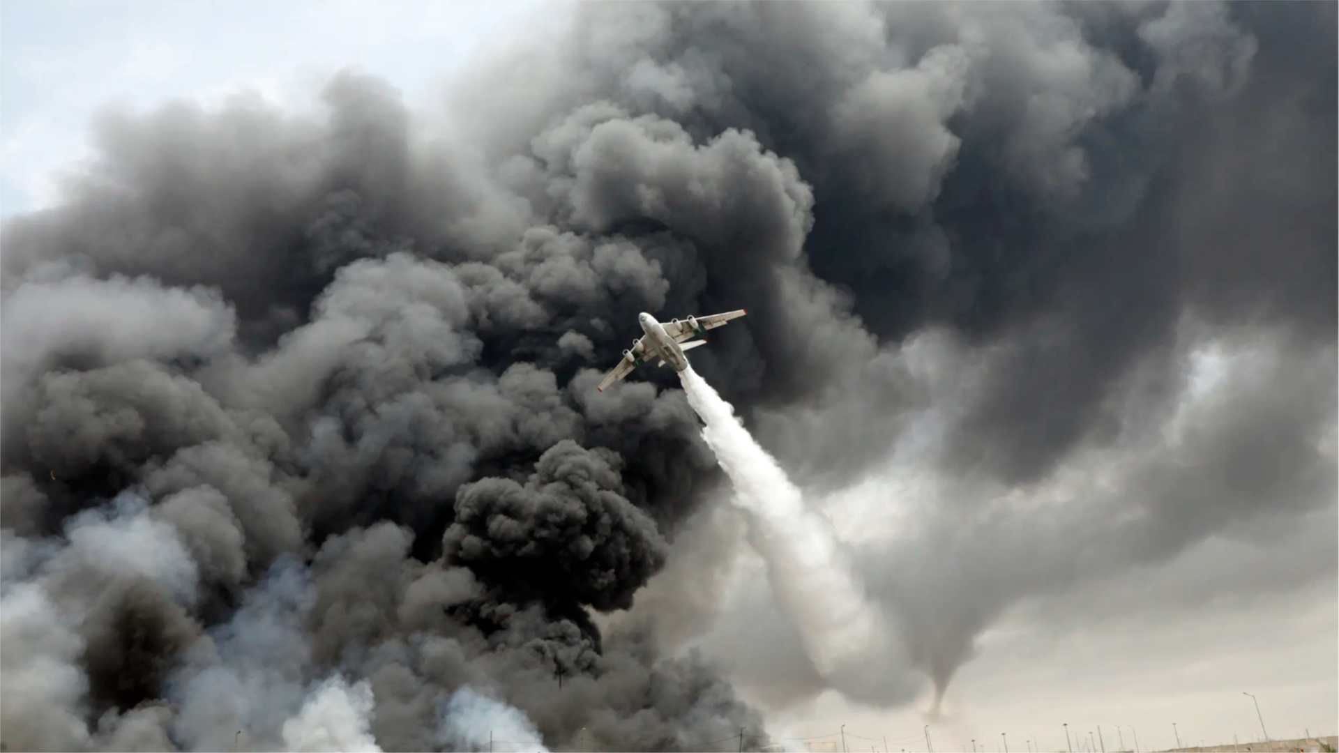 An aircraft drops water at the site of an explosion that occurred a day earlier at the Shahid Rajaee Port dock near Bandar Abbas, Iran.