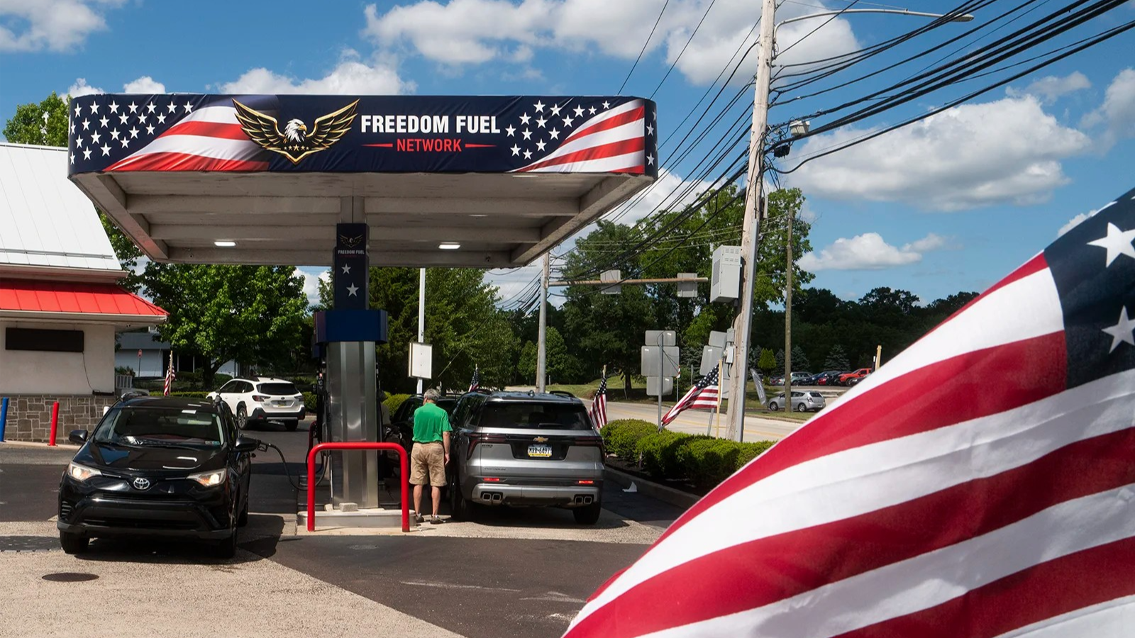 Part of the American flag waves in front of a Freedom Fuel gas station as one person gets gas.