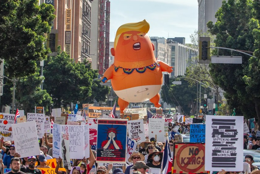 People hold signs followed by a 20-foot-tall helium-filled balloon of Trump wearing a diaper in front of City Hall during a national ‘No Kings’ protest on March 28, 2026, in Los Angeles, Calif