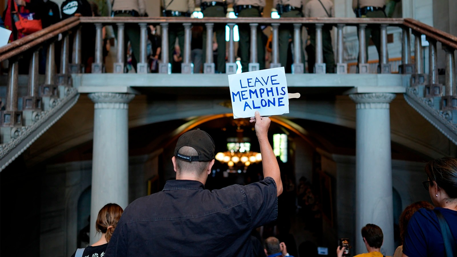 A person with their back toward the camera holds a small sign that says 