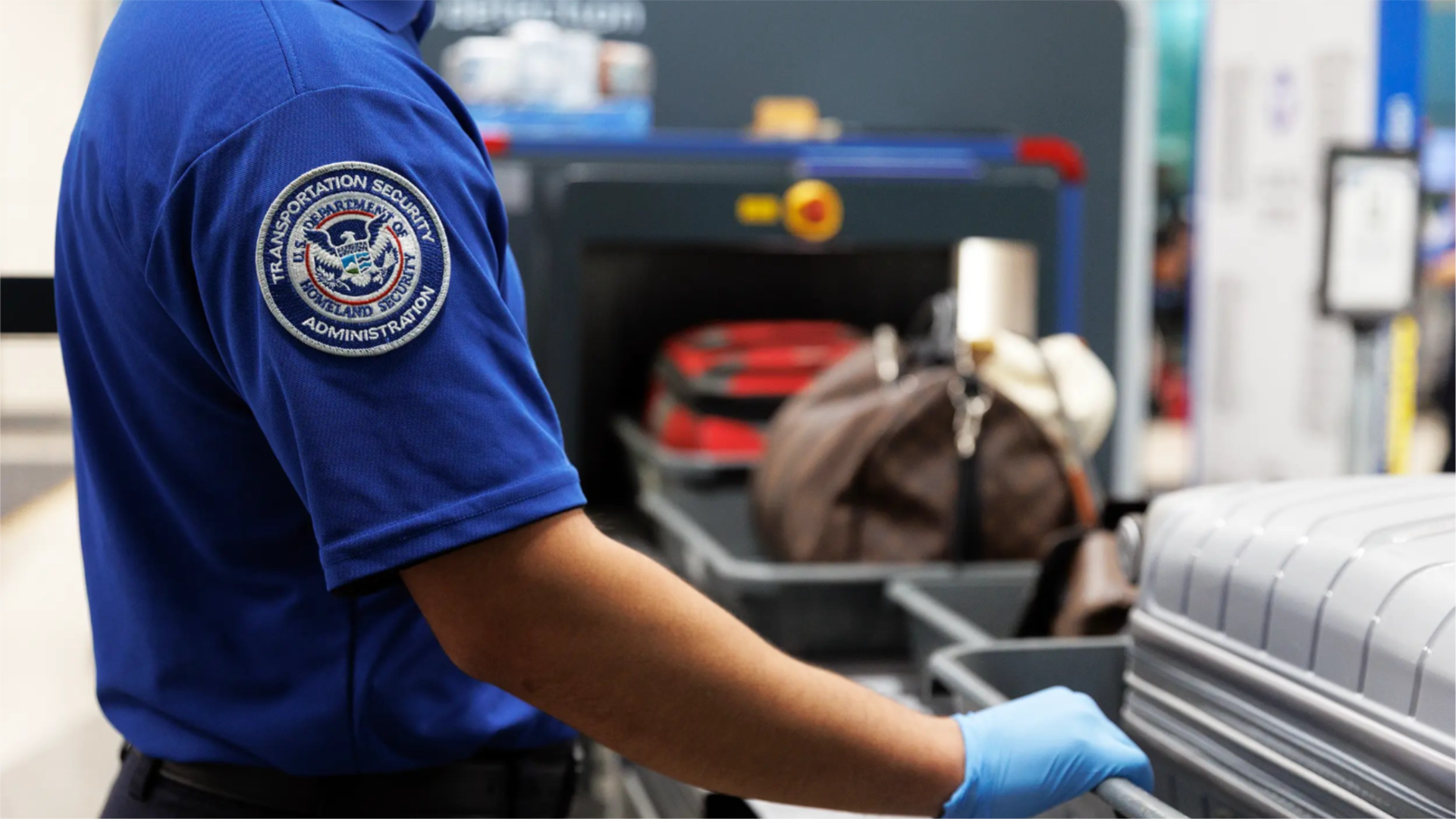 A photo of a TSA agent standing by a conveyor belt at the airport