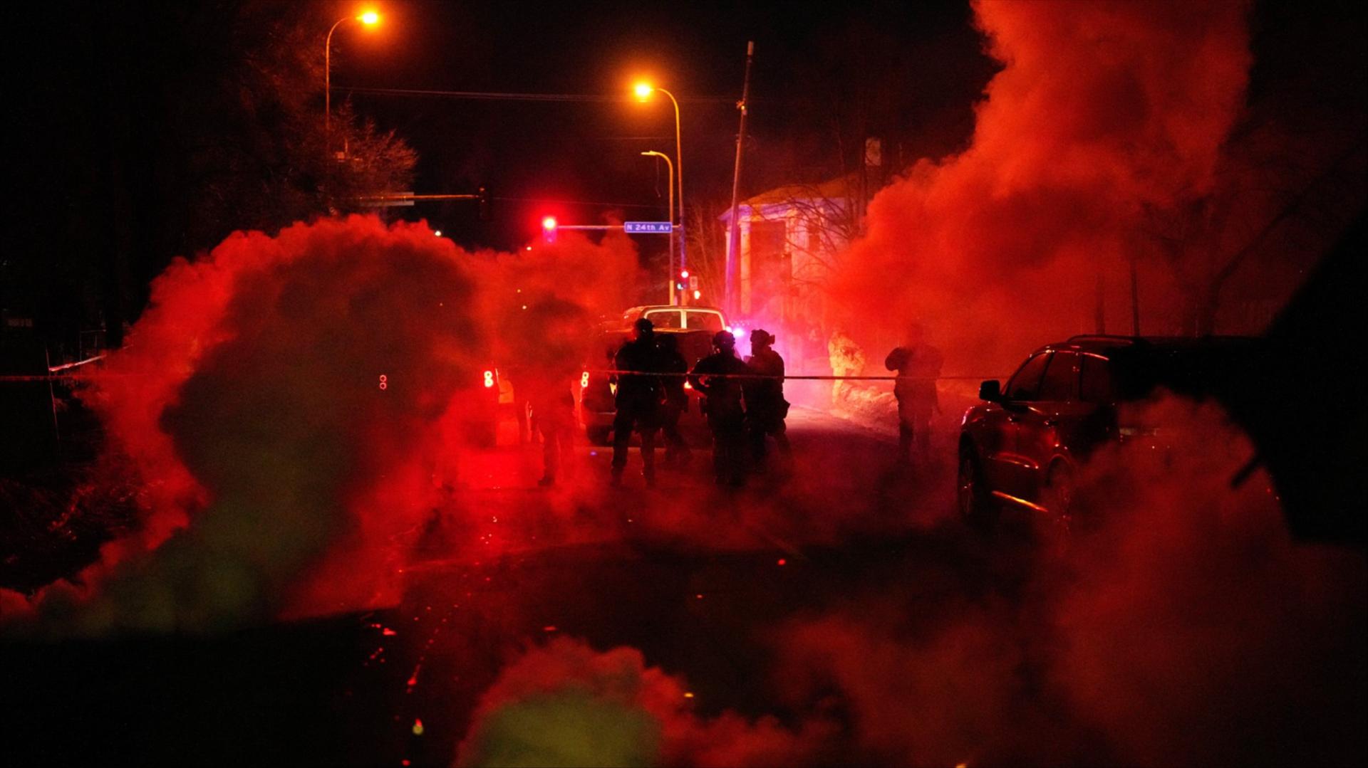Officers are surrounded by tear gas which is illuminated red by nearby lights.
