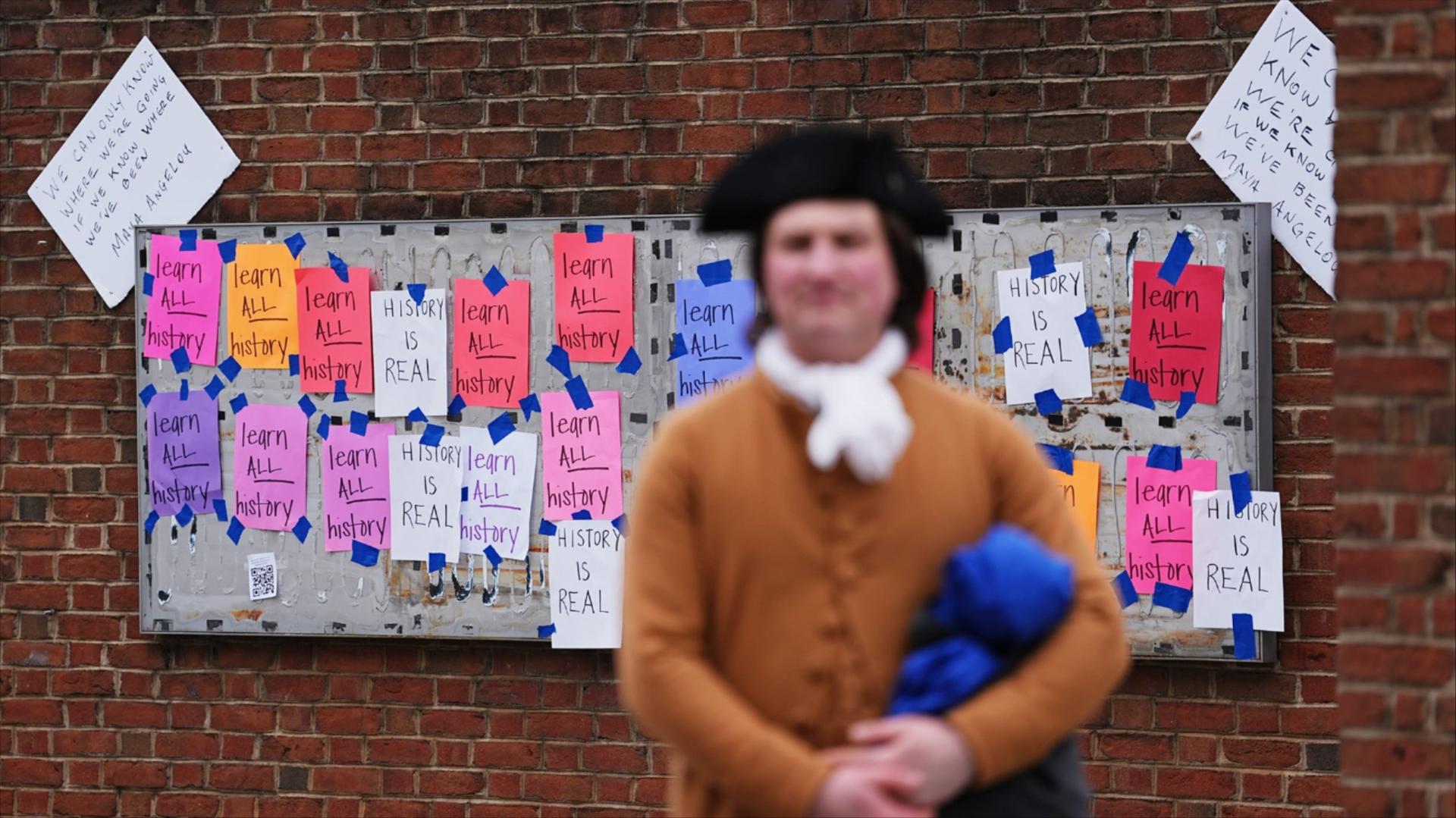 A tour guide stands in front of signs posted on top of an empty panel which used to be part of an exhibit on slavery at the President's House on Jan. 23, 2026, in Philadelphia