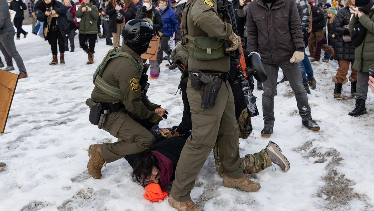 Federal agents pin a protestor on the ground while others document the incident.