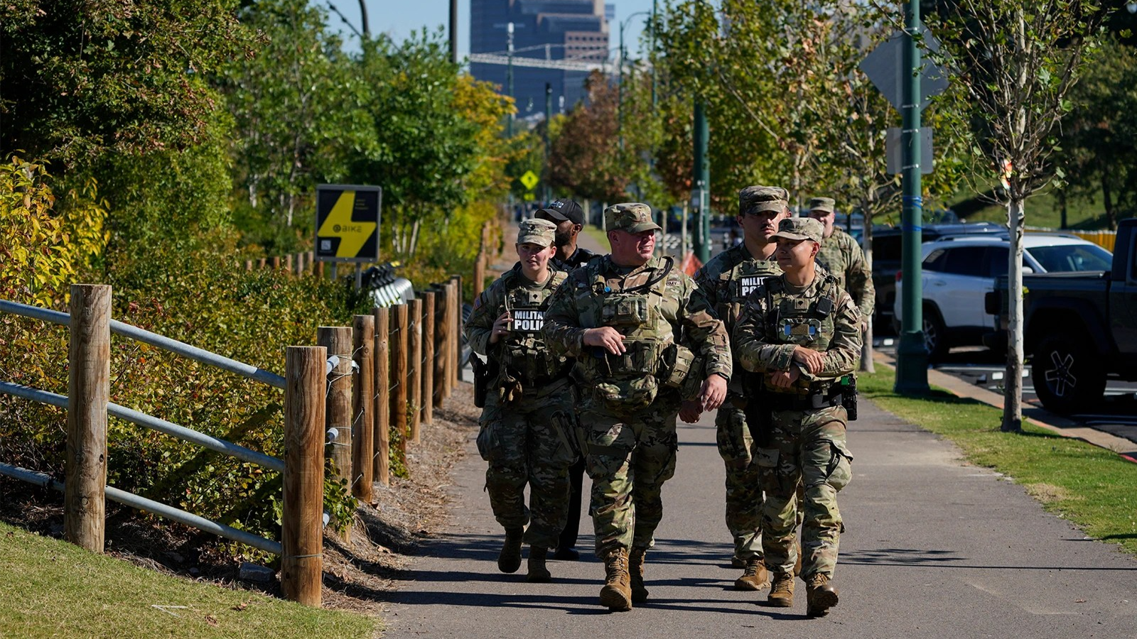 Multiple military members in camouflage and one police officer walk down a street next to a park in Memphis.