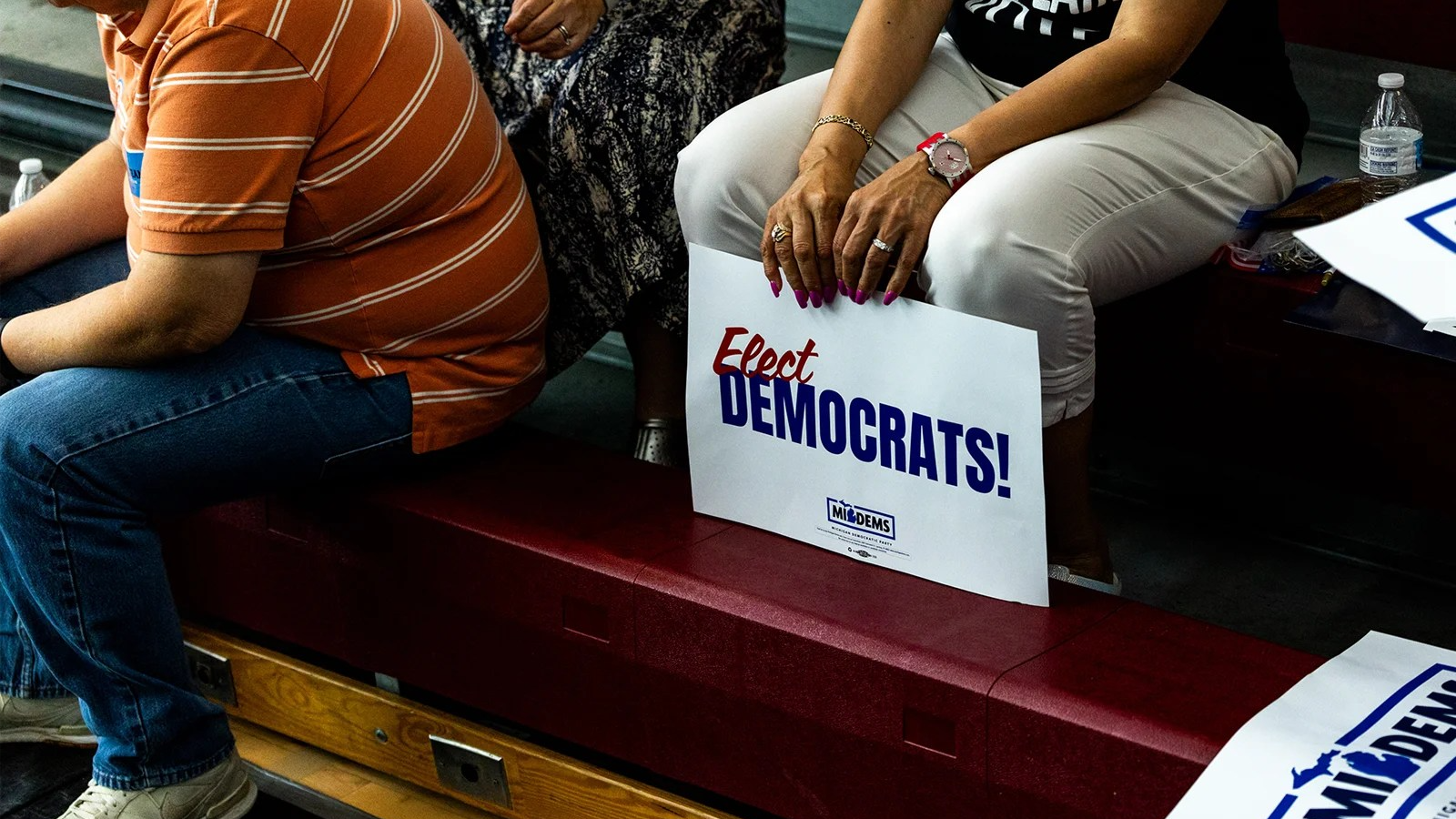 Three people sit as one holds a sign that reads elect democrats.